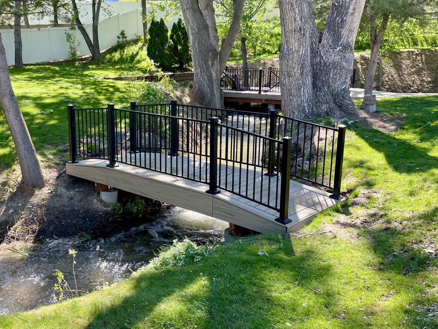 Custom footbridge over stream in lush backyard